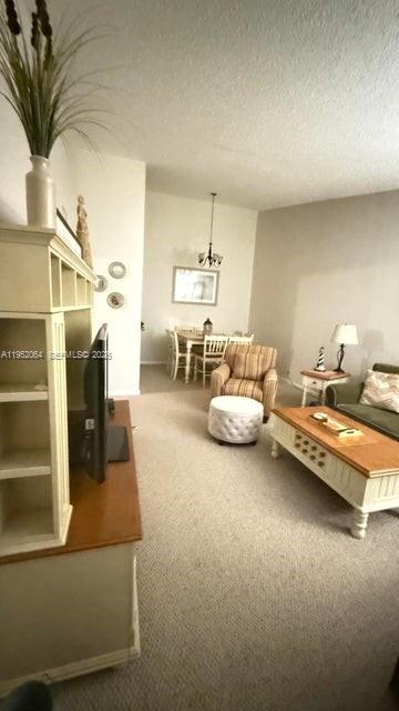 A living room with beige carpet, a wooden coffee table, and a dining area beyond — 6327 Chasewood Dr # G, Jupiter FL 33458, JUPITER, FL
