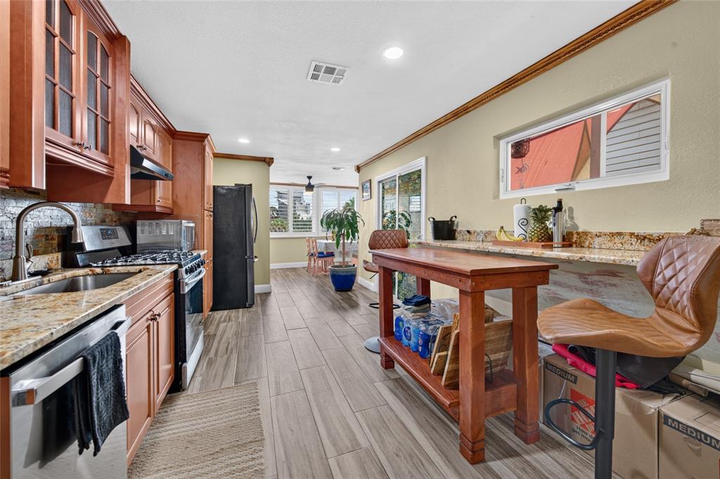 A kitchen features wood cabinets, granite countertops, stainless steel appliances, and a wooden breakfast table — 881 CATFISH AVENUE, NEW SMYRNA BEACH, FL