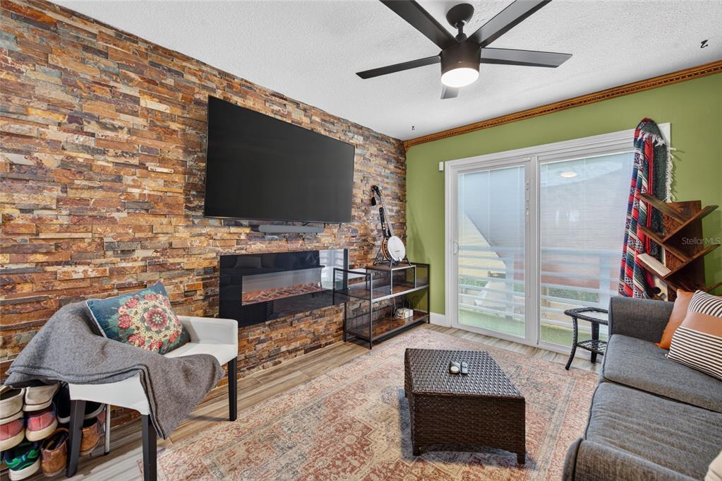 A living room features a stone accent wall with a mounted television and electric fireplace — 881 CATFISH AVENUE, NEW SMYRNA BEACH, FL