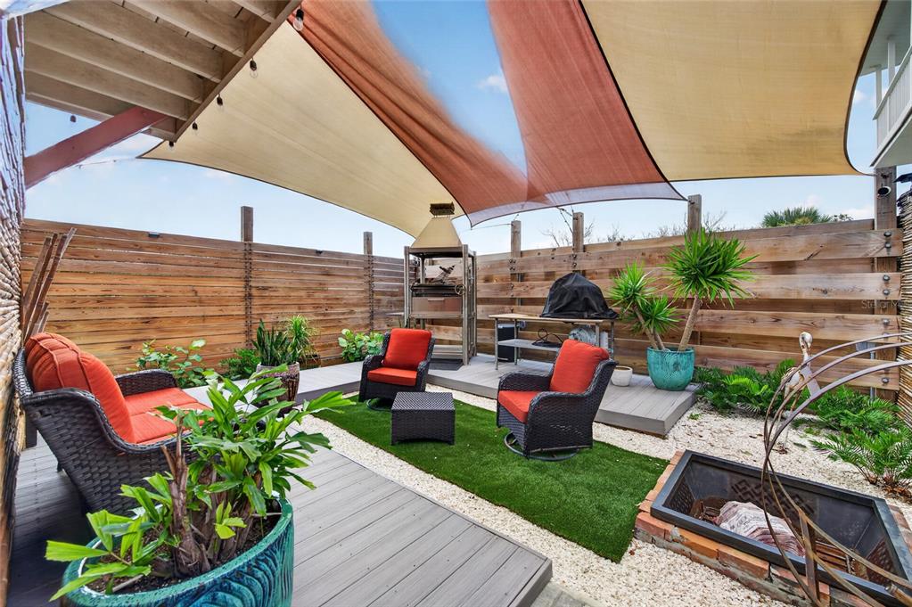 An outdoor patio features a shade sail, wicker furniture with orange cushions, and a fire pit — 881 CATFISH AVENUE, NEW SMYRNA BEACH, FL