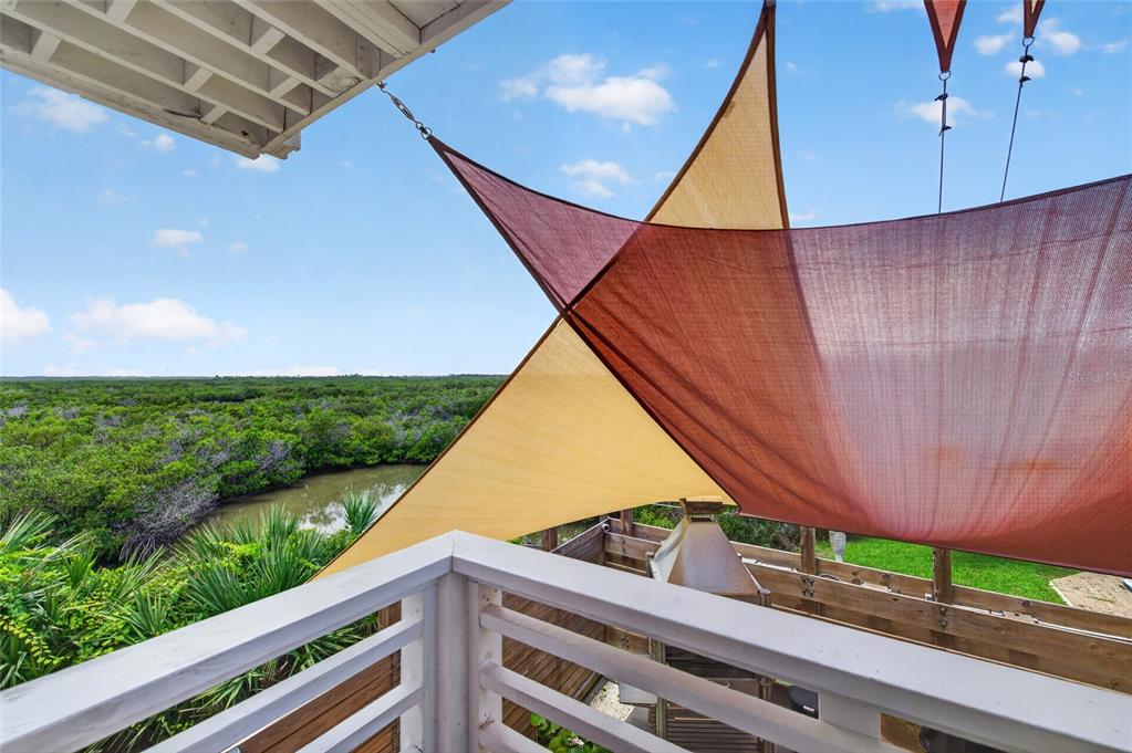 A wooden balcony overlooks a marshy landscape under large, overlapping tan and maroon shade sails — 881 CATFISH AVENUE, NEW SMYRNA BEACH, FL