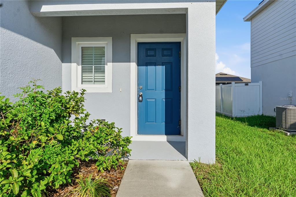 A blue front door is set into a light gray exterior wall beside a window — 1530 FINNIGAN CIRCLE, HAINES CITY, FL