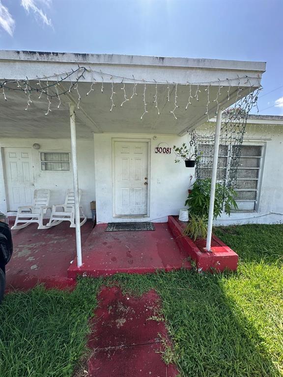 A white house exterior features a red porch, two white chairs, and string lights — 30081 SW 148TH AVENUE, HOMESTEAD, FL