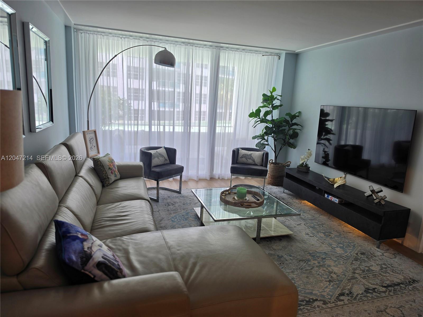 A living room features a leather sectional, glass coffee table, and a wall-mounted television — 5151 Collins Ave # 429, Miami Beach FL 33140, MIAMI BEACH, FL