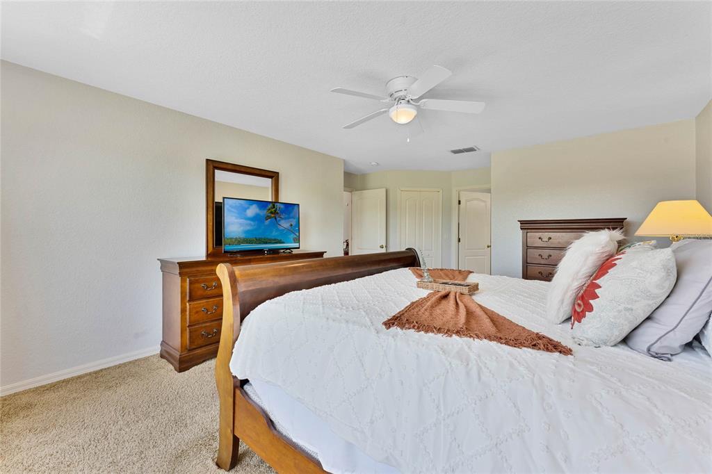 A bedroom features a wooden bed frame, a dresser with a television, and carpeted flooring — 606 BIRKDALE STREET, DAVENPORT, FL