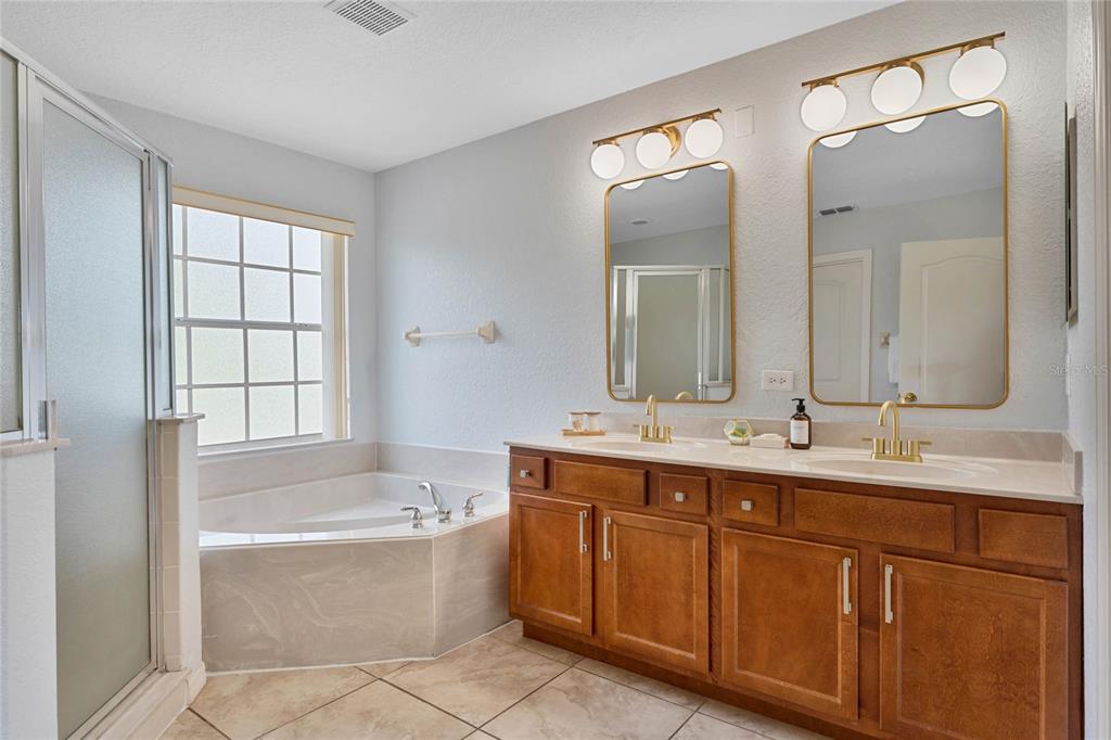 A bathroom features a double vanity with wood cabinets, gold fixtures, and a corner soaking tub — 606 BIRKDALE STREET, DAVENPORT, FL