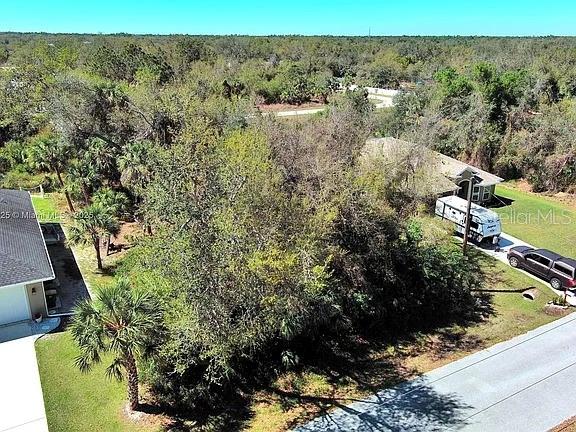 An aerial view shows a wooded lot between two houses with a parked trailer and truck — 205 FERDON CIRCLE, PORT CHARLOTTE, FL