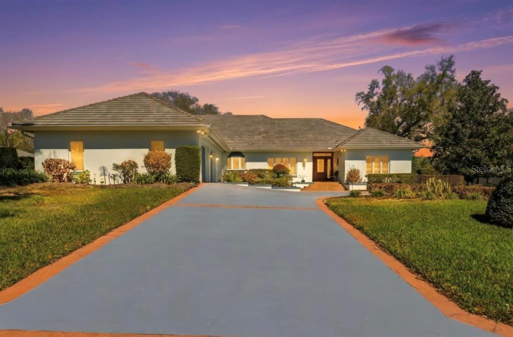 A single-story house with a gray tile roof and a long, paved driveway at sunset — 133 ARROWHEAD LANE, HAINES CITY, FL