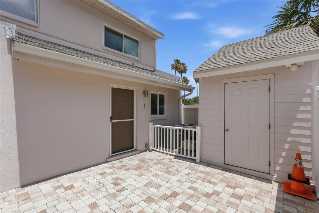 A paved patio sits between a two-story residential building and a small detached storage shed — 3120 BEACH BOULEVARD S UNIT 1, GULFPORT, FL