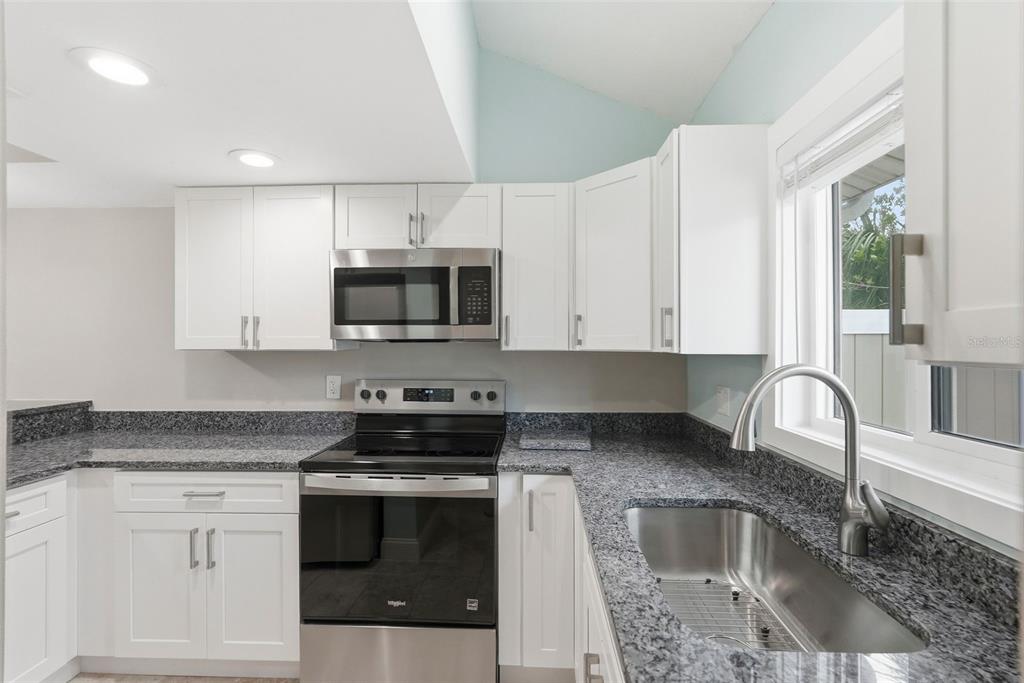 A kitchen with white cabinets, granite countertops, stainless steel appliances, and a stainless steel sink — 3120 BEACH BOULEVARD S UNIT 1, GULFPORT, FL