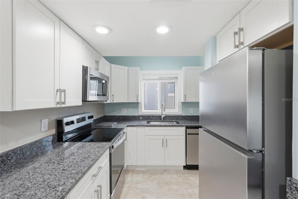 A kitchen features white cabinets, granite countertops, stainless steel appliances, and light blue walls — 3120 BEACH BOULEVARD S UNIT 1, GULFPORT, FL