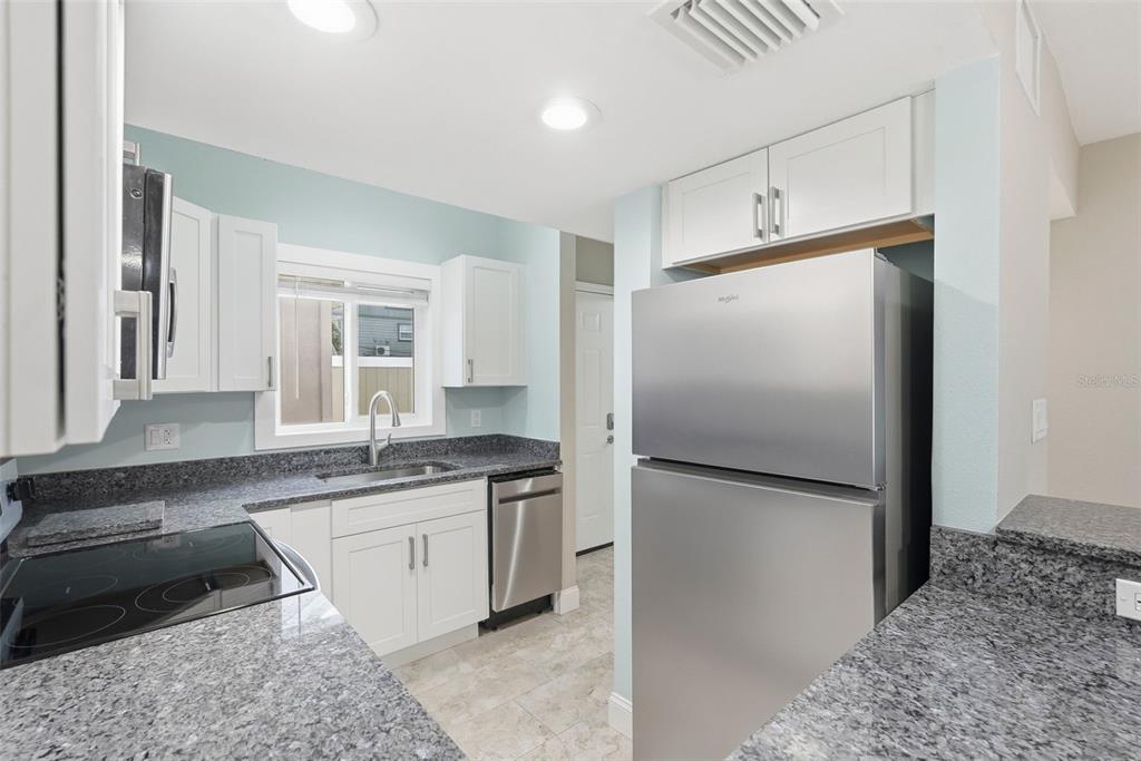 A kitchen features white cabinets, granite countertops, stainless steel appliances, and light blue walls — 3120 BEACH BOULEVARD S UNIT 1, GULFPORT, FL