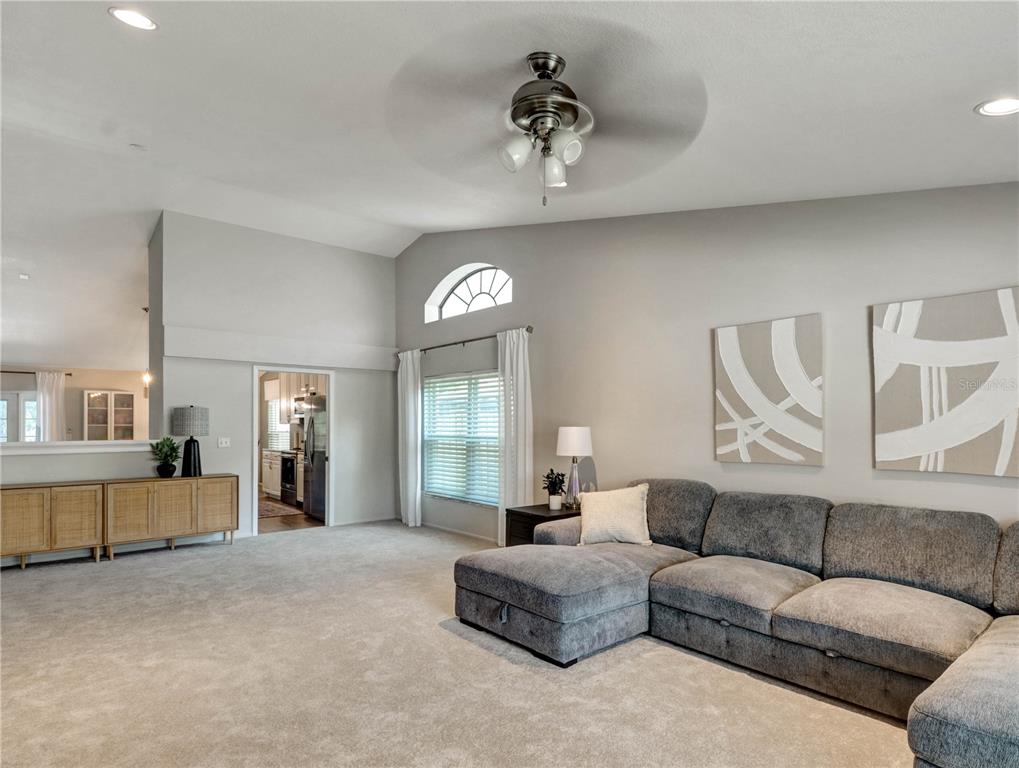 A living room features a gray sectional sofa, neutral carpeting, and a ceiling fan — 12004 STEPPINGSTONE BOULEVARD, TAMPA, FL