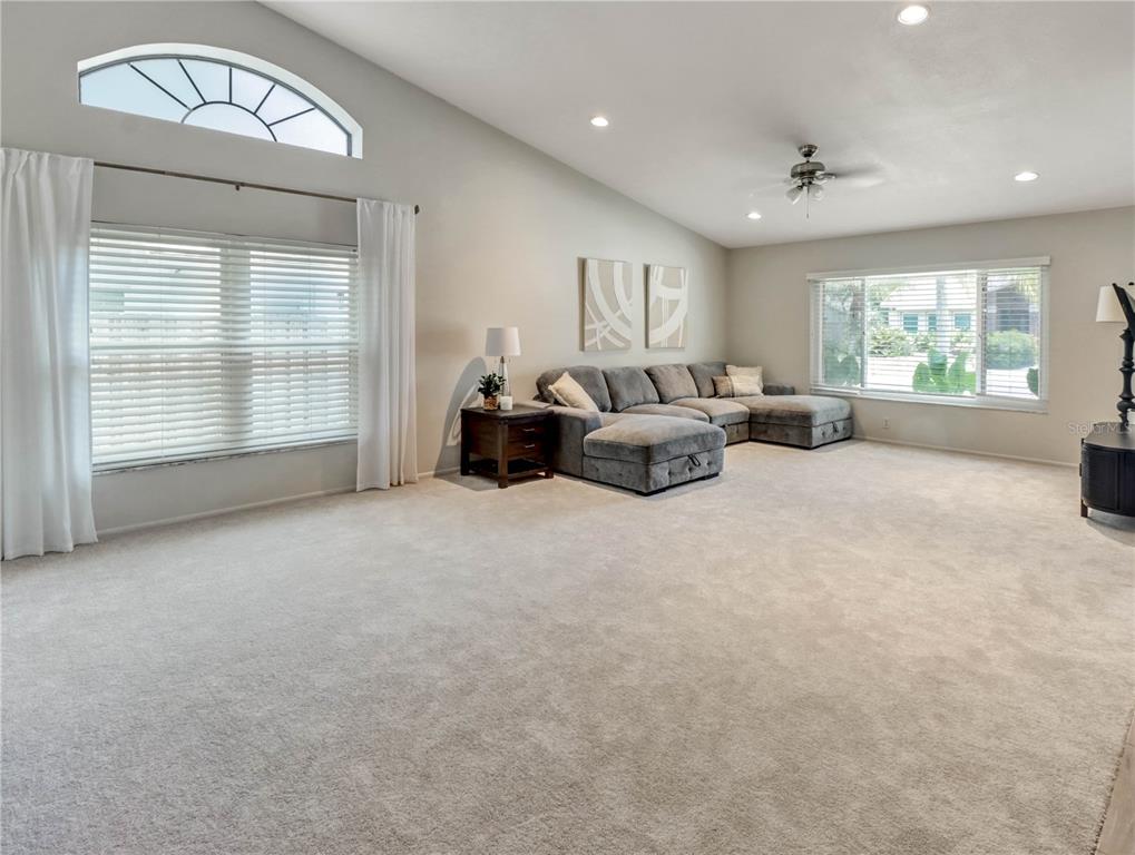 A spacious living room features neutral carpeting, a large gray sectional sofa, and vaulted ceilings — 12004 STEPPINGSTONE BOULEVARD, TAMPA, FL