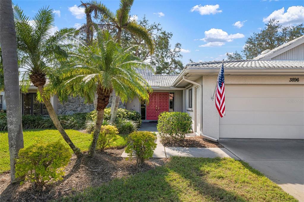 A single-story house features a red double front door, a garage, and palm trees — 3896 WILSHIRE DRIVE UNIT 11, SARASOTA, FL