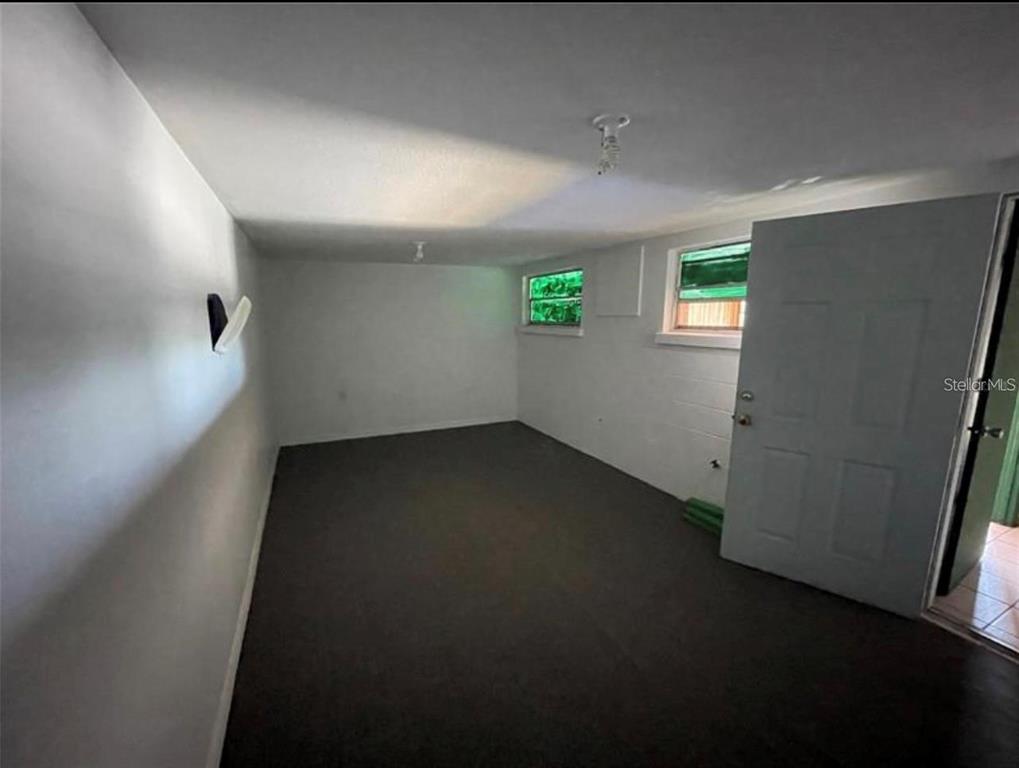 An empty room with white walls, dark carpeting, two windows, and a white door — 1614 9TH STREET W, BRADENTON, FL