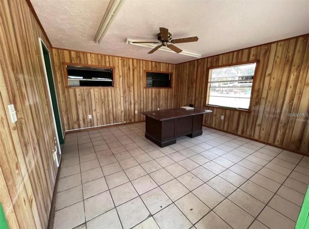 An office room features wood-paneled walls, a tile floor, a ceiling fan, and a desk — 1614 9TH STREET W, BRADENTON, FL