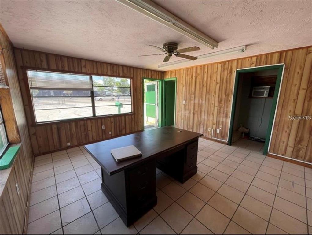 An office room features wood-paneled walls, tile flooring, a central desk, and a ceiling fan — 1614 9TH STREET W, BRADENTON, FL