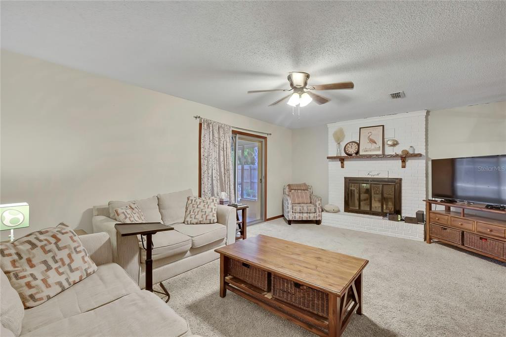 A living room features a white brick fireplace, a ceiling fan, and beige carpet — 1931 SE 39TH STREET, OCALA, FL