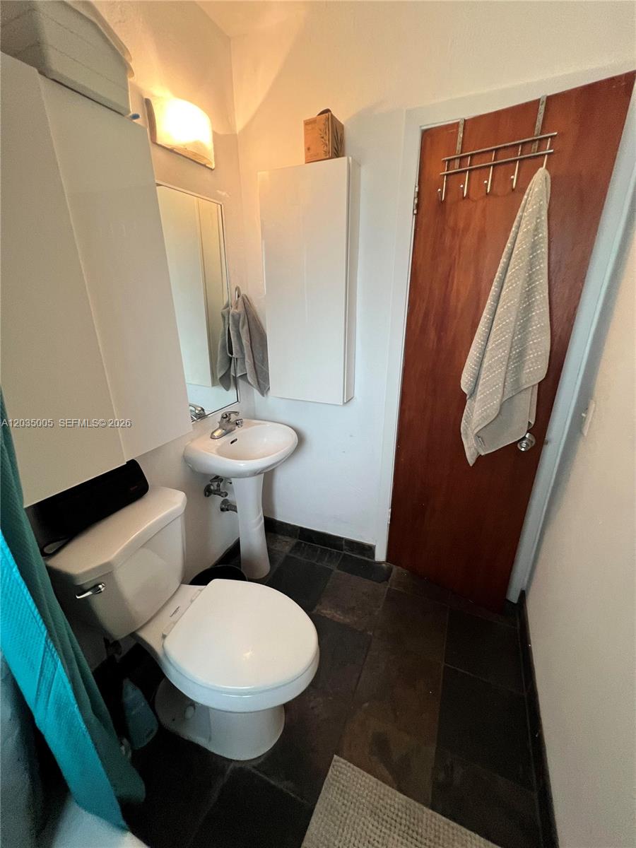 This bathroom features a pedestal sink, a toilet, and a wooden door with a rack — 8845 NE 8TH COURT # 2, Miami FL 33138, MIAMI, FL
