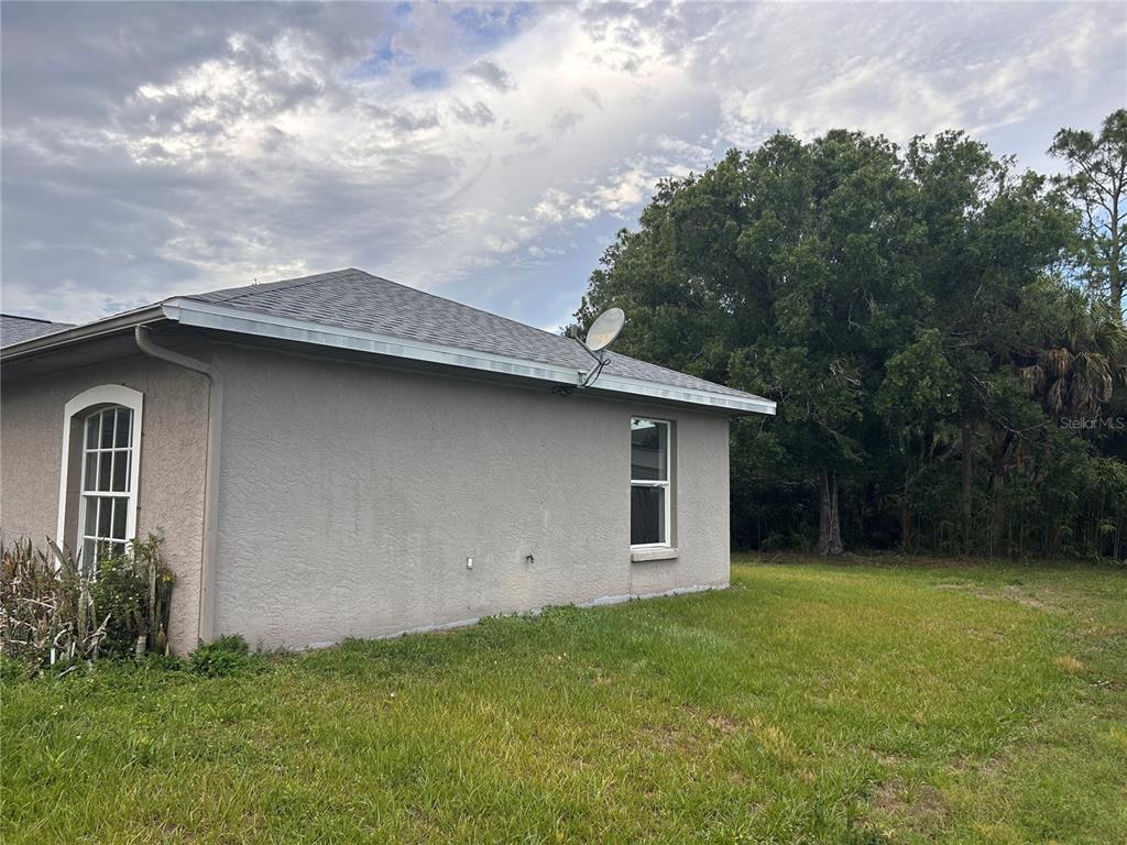 The exterior side view of a house features a stucco wall, two windows, and a satellite dish — 2514 AFFINITY LANE, NORTH PORT, FL