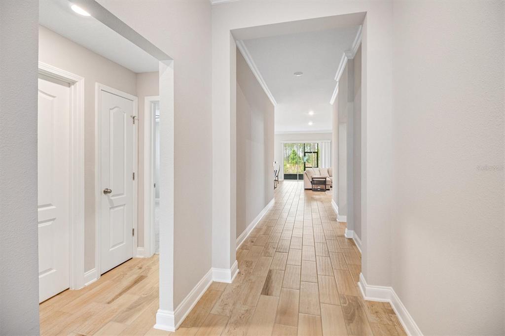 A hallway with light wood-look tile flooring leads toward a bright living area — 7 SUMMERWOOD ROAD N, PALM COAST, FL