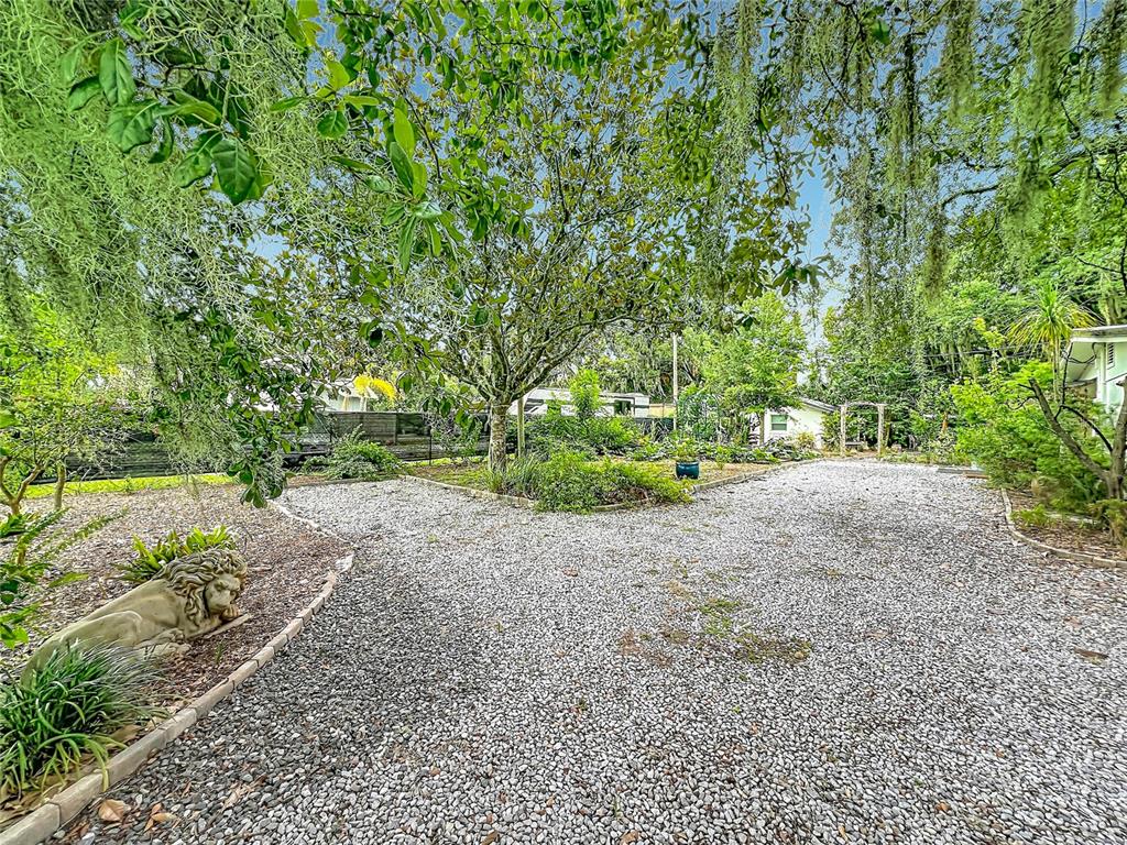 A gravel driveway leads to a landscaped yard with a stone lion statue and trees — 3851 S SANFORD AVENUE, SANFORD, FL