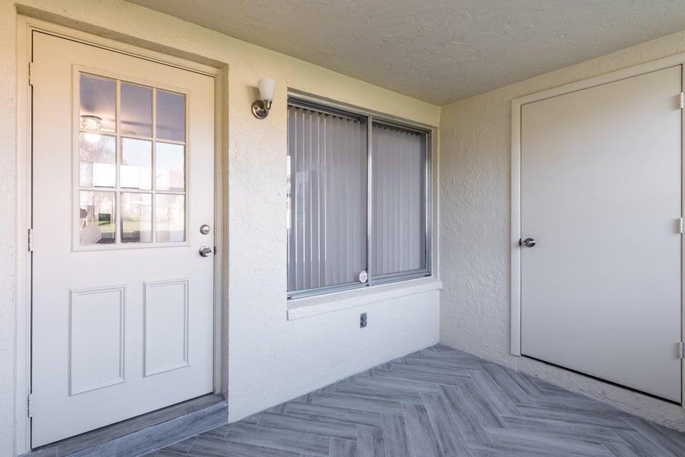 A covered entryway with a white door, a window with vertical blinds, and herringbone flooring — 4765 Sable Pine Circle # B1, West Palm Beach FL 33417, WEST PALM BEACH, FL