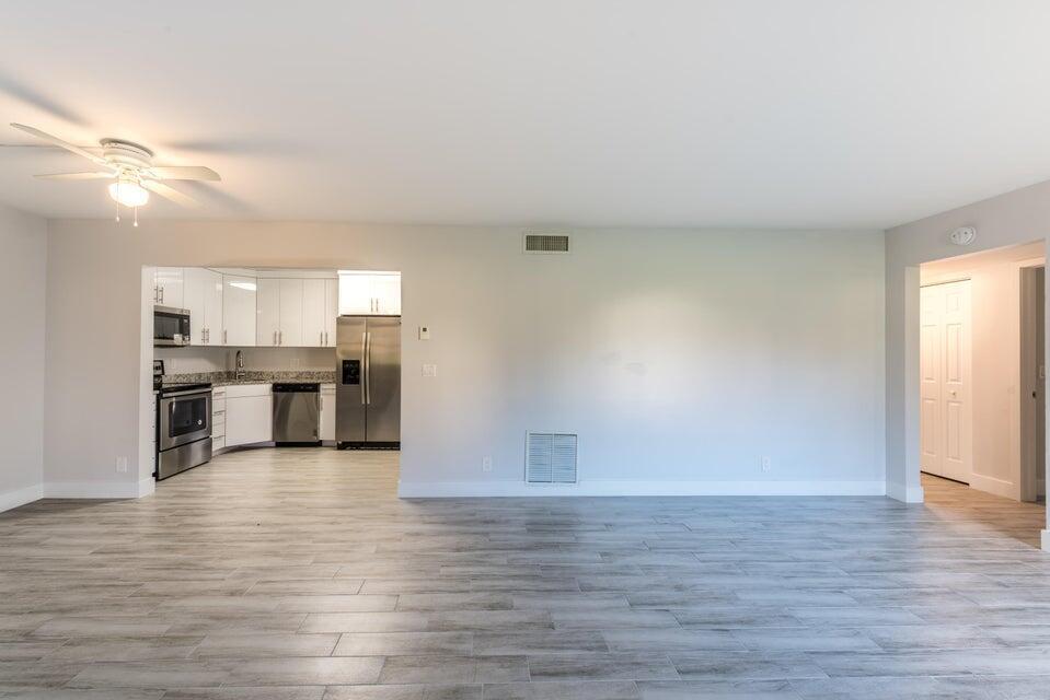 A spacious living area with light gray wood-look tile flooring leads into a modern kitchen — 4765 Sable Pine Circle # B1, West Palm Beach FL 33417, WEST PALM BEACH, FL