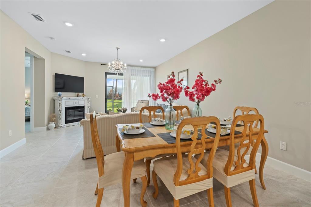 A dining area with a wooden table and chairs sits before a living room fireplace — 14586 MOSSY PINE COURT, NOKOMIS, FL