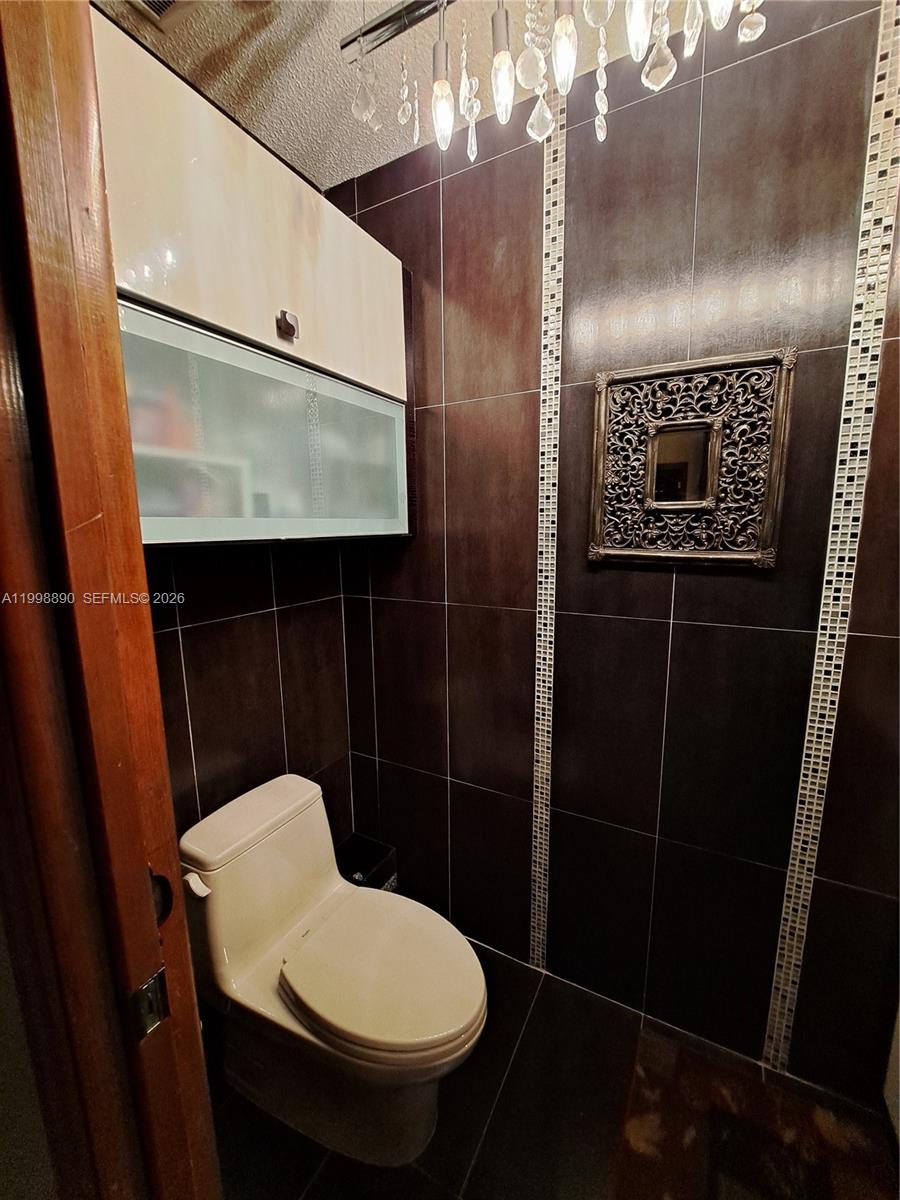 A small bathroom features dark tiled walls, a toilet, and a wall-mounted cabinet — 14527 SW 106th Ter, Miami FL 33186, MIAMI, FL