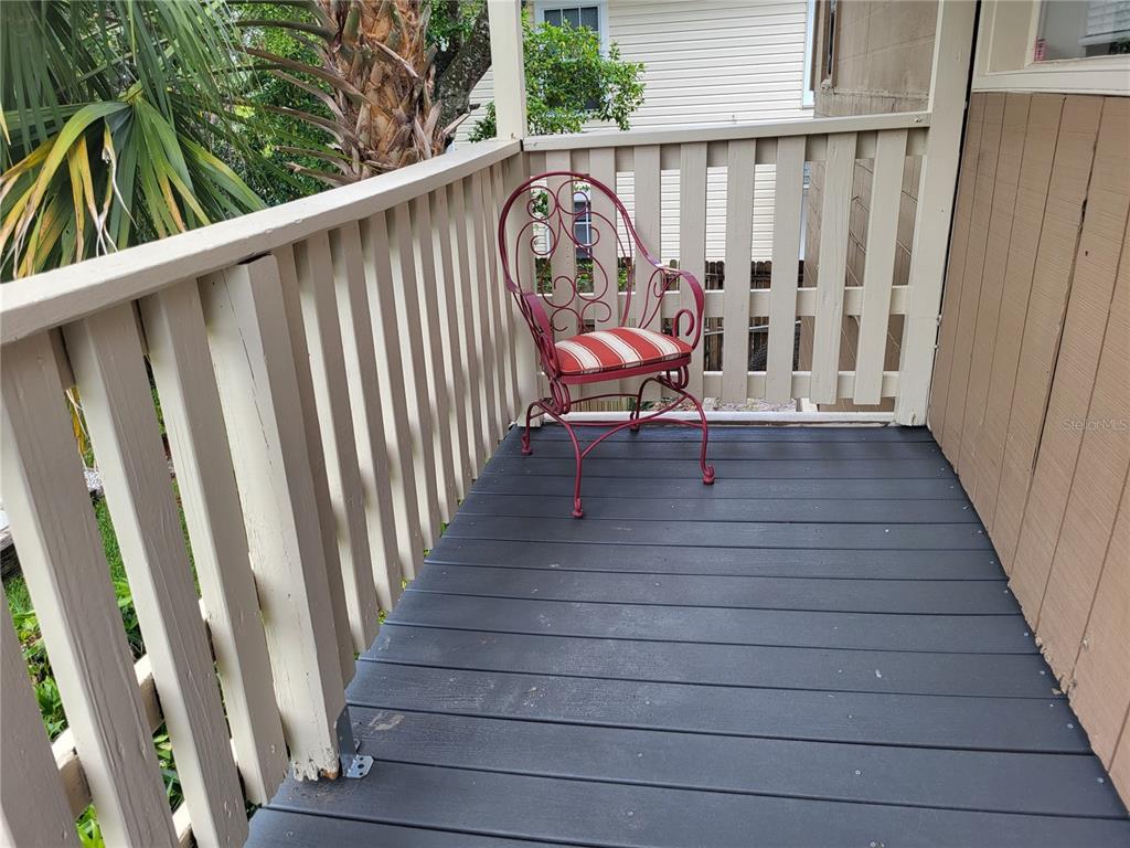 A red metal chair with a striped cushion sits on a gray wooden deck balcony — 211 W BAY AVENUE UNIT A, LONGWOOD, FL