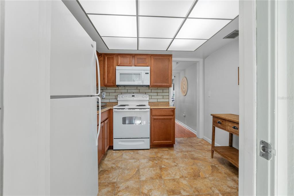 A kitchen with wood cabinets, white appliances, a tiled backsplash, and a drop ceiling — 7801 11TH STREET N UNIT 302, ST PETERSBURG, FL