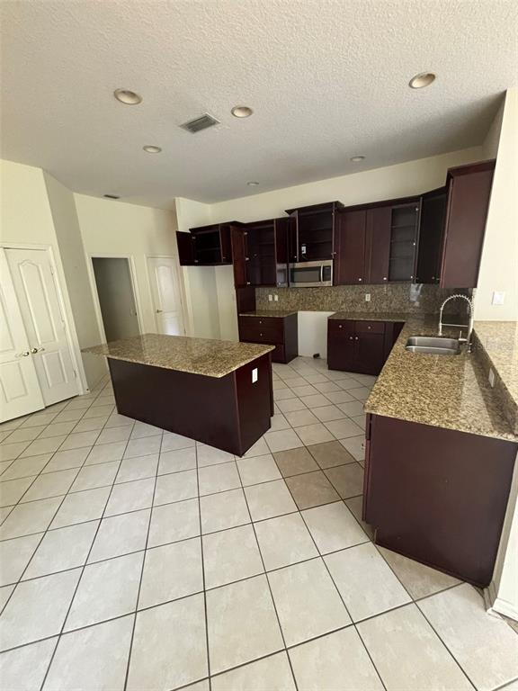 A kitchen features dark wood cabinets, granite countertops, a center island, and tile flooring — 5141 SILVER CHARM TERRACE, ZEPHYRHILLS, FL