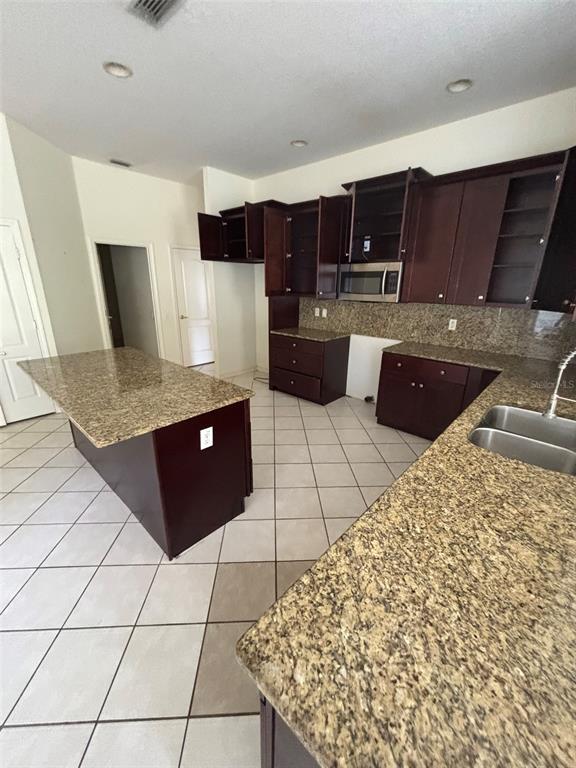 A kitchen features dark wood cabinets, granite countertops, a center island, and tiled flooring — 5141 SILVER CHARM TERRACE, ZEPHYRHILLS, FL