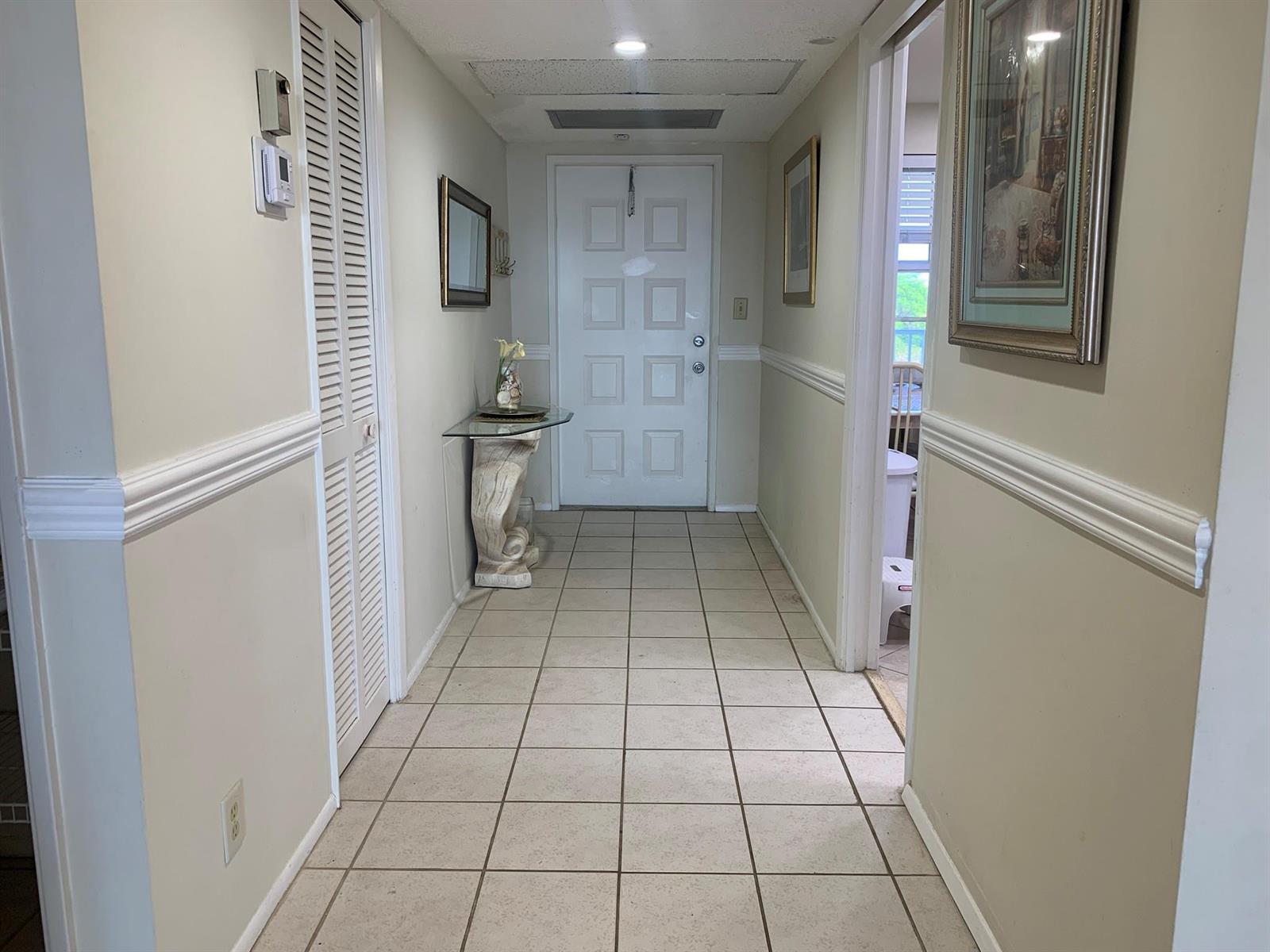 A tiled hallway leads to a white front door with a glass console table nearby — 3499 Oaks Way # 607, Pompano Beach FL 33069, POMPANO BEACH, FL