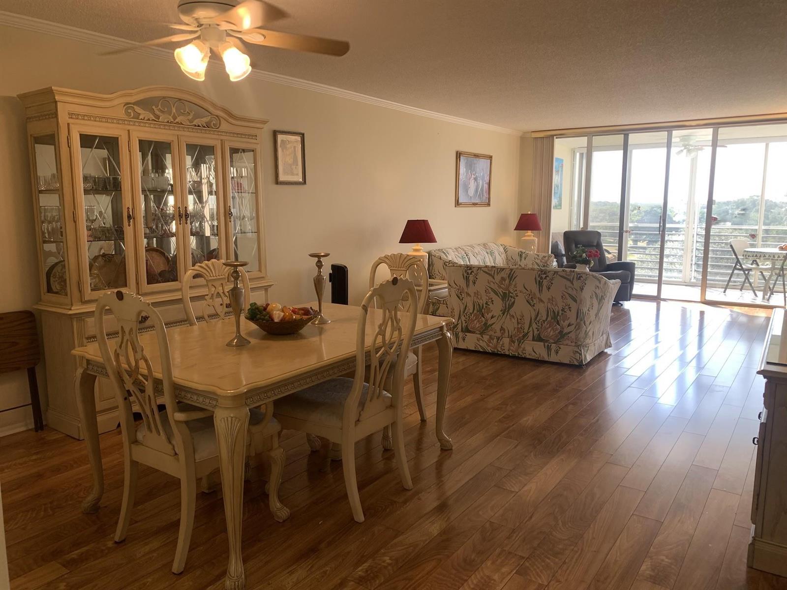 A dining area and living room with hardwood floors, floral furniture, and a glass balcony door — 3499 Oaks Way # 607, Pompano Beach FL 33069, POMPANO BEACH, FL