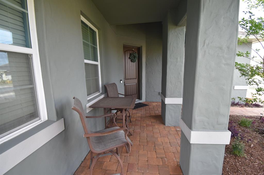 A covered front porch features a brick paver floor, two chairs, a table, and columns — 709 CALABRIA WAY, HOWEY IN THE HILLS, FL
