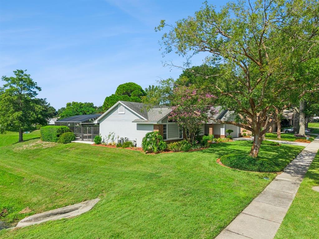 A single-story house with a screened pool enclosure sits on a grassy lot with trees — 1129 CLIMBING ROSE DRIVE, OCOEE, FL