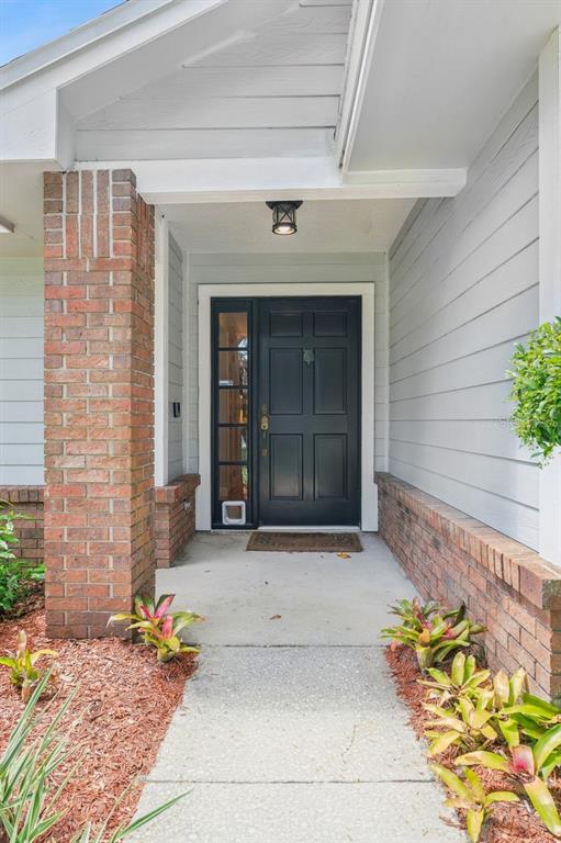 A front entryway features a black door with a sidelight, brick columns, and landscaped beds — 1129 CLIMBING ROSE DRIVE, OCOEE, FL