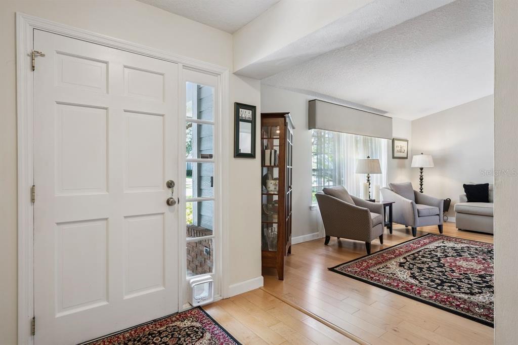 A white front door opens into a living room with hardwood floors and two armchairs — 1129 CLIMBING ROSE DRIVE, OCOEE, FL