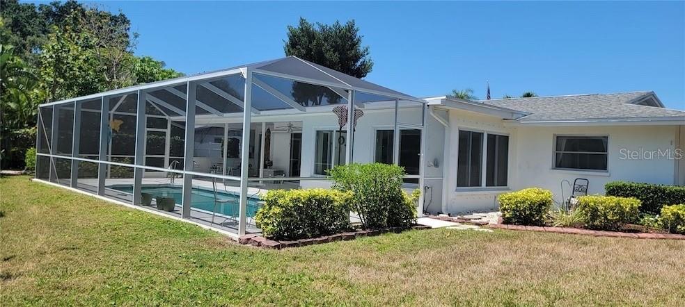 A house with a screened-in pool enclosure and a grassy backyard under a clear sky — 6307 FORDHAM PLACE, BRADENTON, FL