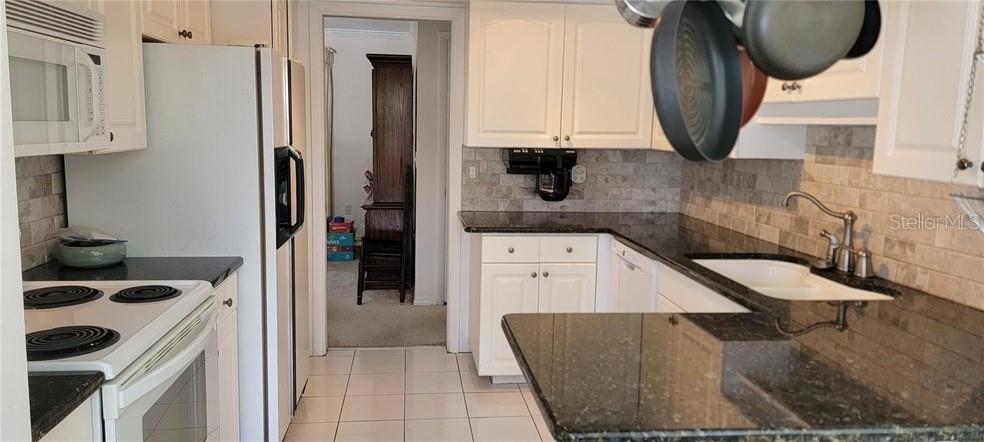 A kitchen features white cabinets, dark granite countertops, stainless steel appliances, and a tiled backsplash — 6307 FORDHAM PLACE, BRADENTON, FL