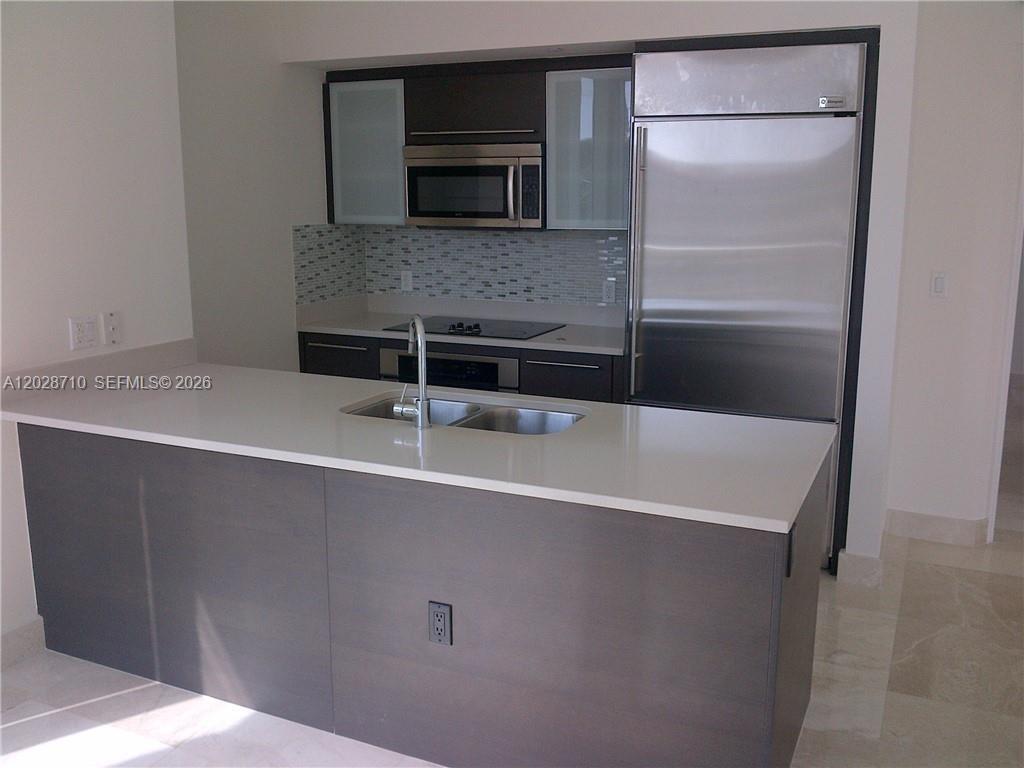 A modern kitchen features a dark wood island, white countertops, and stainless steel appliances — 55 SE 6th St # 1502, Miami FL 33131, MIAMI, FL