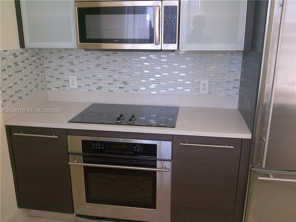 A modern kitchen features dark wood cabinetry, stainless steel appliances, and a white quartz island — 55 SE 6th St # 1502, Miami FL 33131, MIAMI, FL