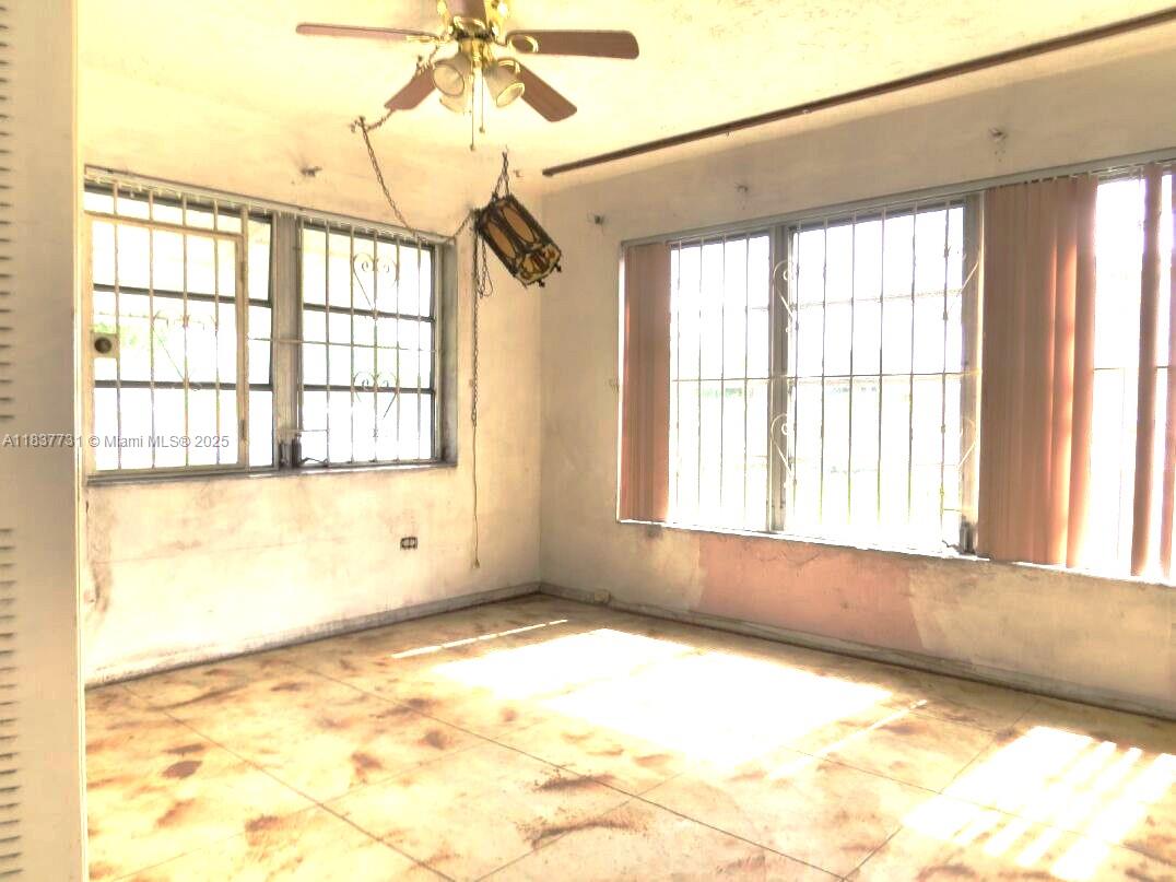 An empty room features tiled floors, barred windows, and a ceiling fan with a hanging lantern — 525 NW 16th St, Pompano Beach FL 33060, POMPANO BEACH, FL