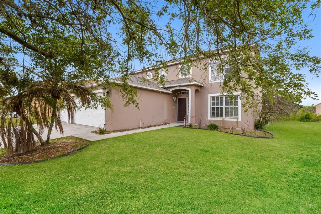 A two-story tan house with a white garage and a green lawn under tree branches — 2361 ANDREWS VALLEY DRIVE, KISSIMMEE, FL