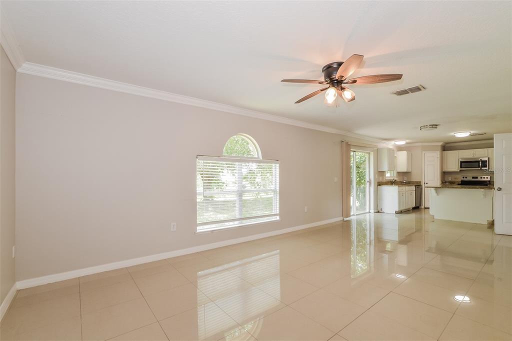 A bright living room with beige tile floors, a ceiling fan, and an adjacent kitchen — 2361 ANDREWS VALLEY DRIVE, KISSIMMEE, FL
