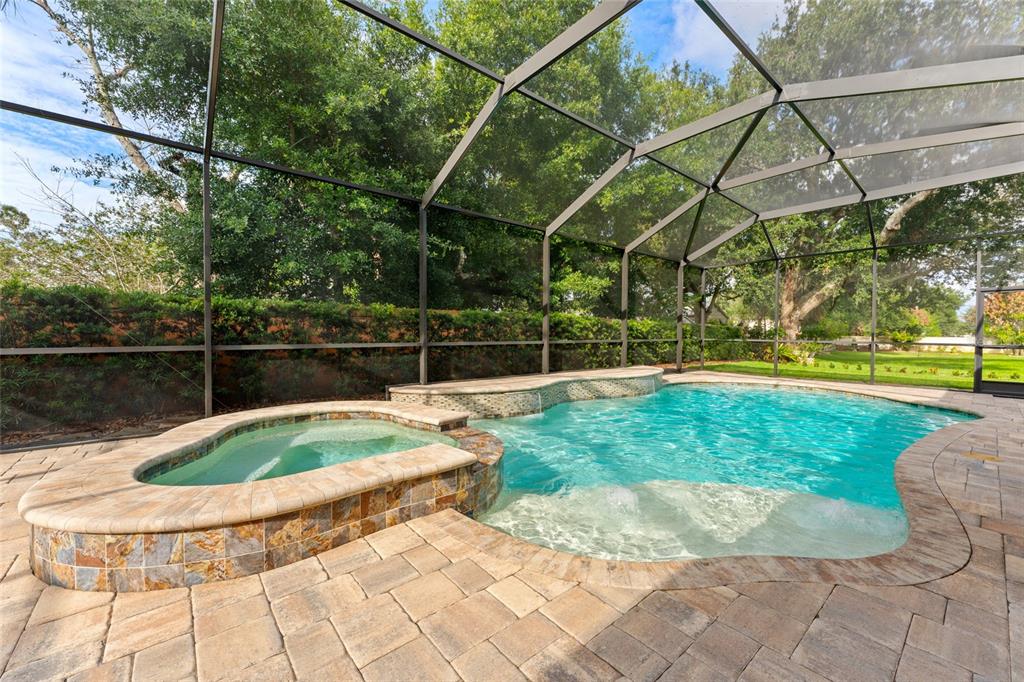 A screened-in swimming pool and attached hot tub with stone tile accents and paver decking — 509 VINTAGE WAY, BRANDON, FL