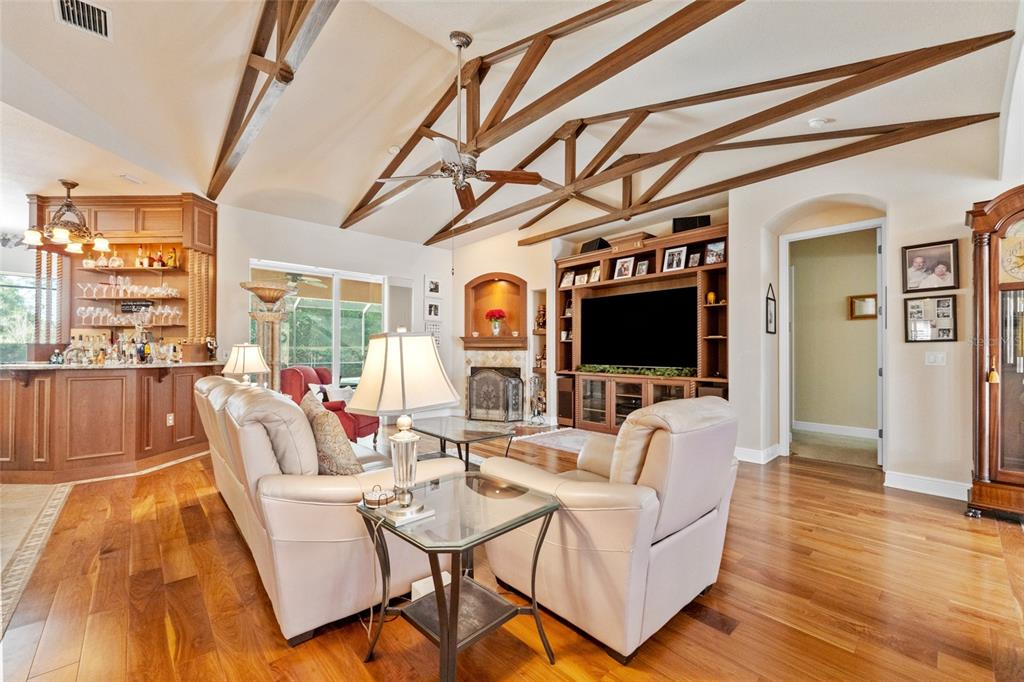 A living room features vaulted wood-beamed ceilings, hardwood floors, a built-in entertainment center, and bar — 509 VINTAGE WAY, BRANDON, FL